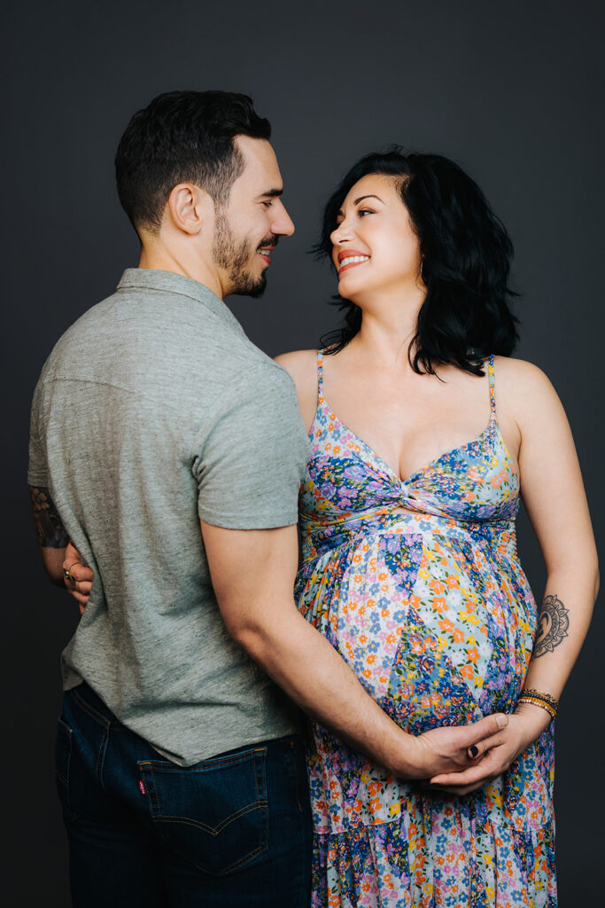 A happy expecting couple stand smiling and holding each other in a studio after a prenatal massage in Cambridge, MA