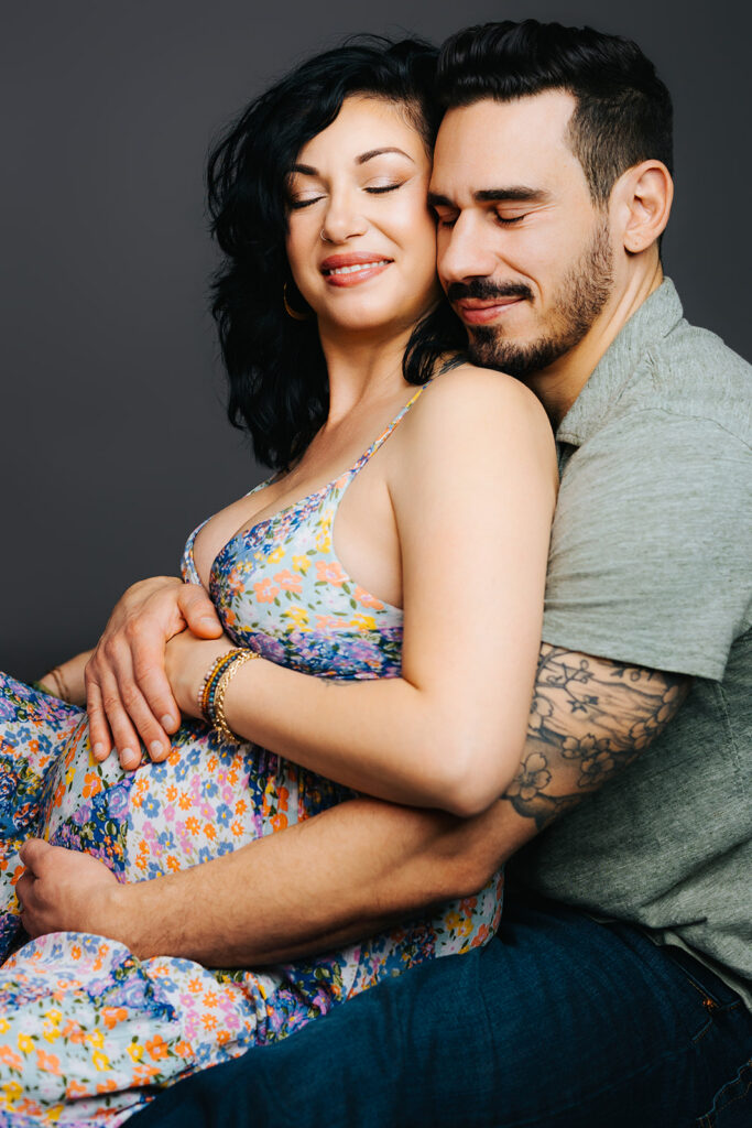A happy pregnant couple snuggles with eyes closed and hands on the bump in a studio after enjoying a prenatal massage in Cambridge, MA