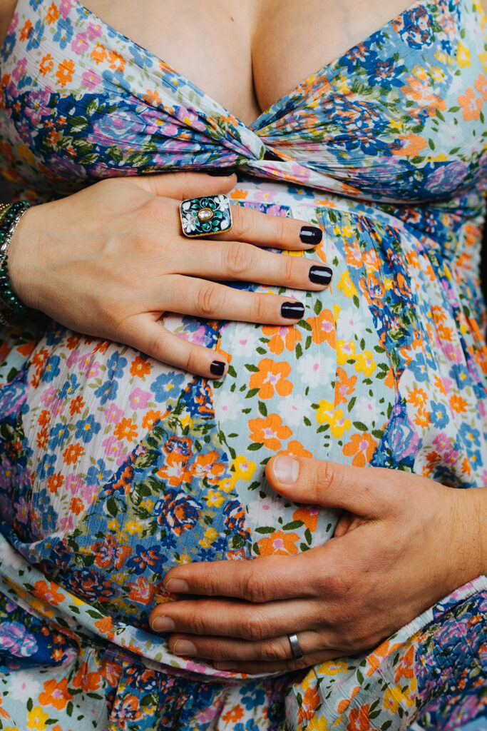 Details of mom and dad's hands on the bump in a bright colorful flower print maternity gown after a prenatal massage in Cambridge, MA