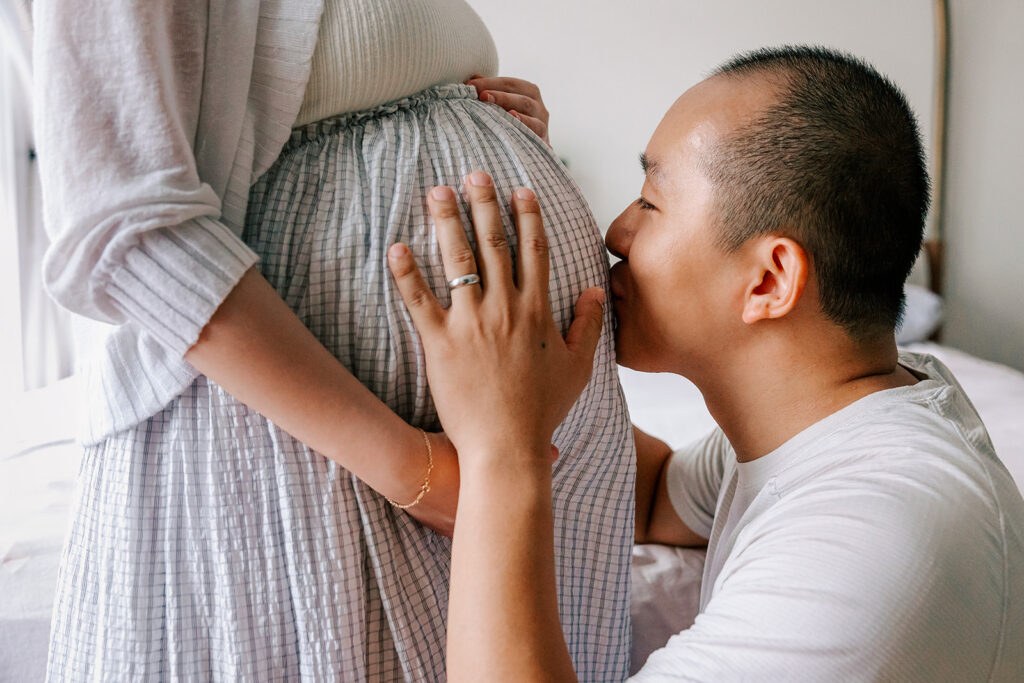 A soon to be father kisses his wife's bump with his hand resting on it before looking for baby shower venues in cambridge, MA.