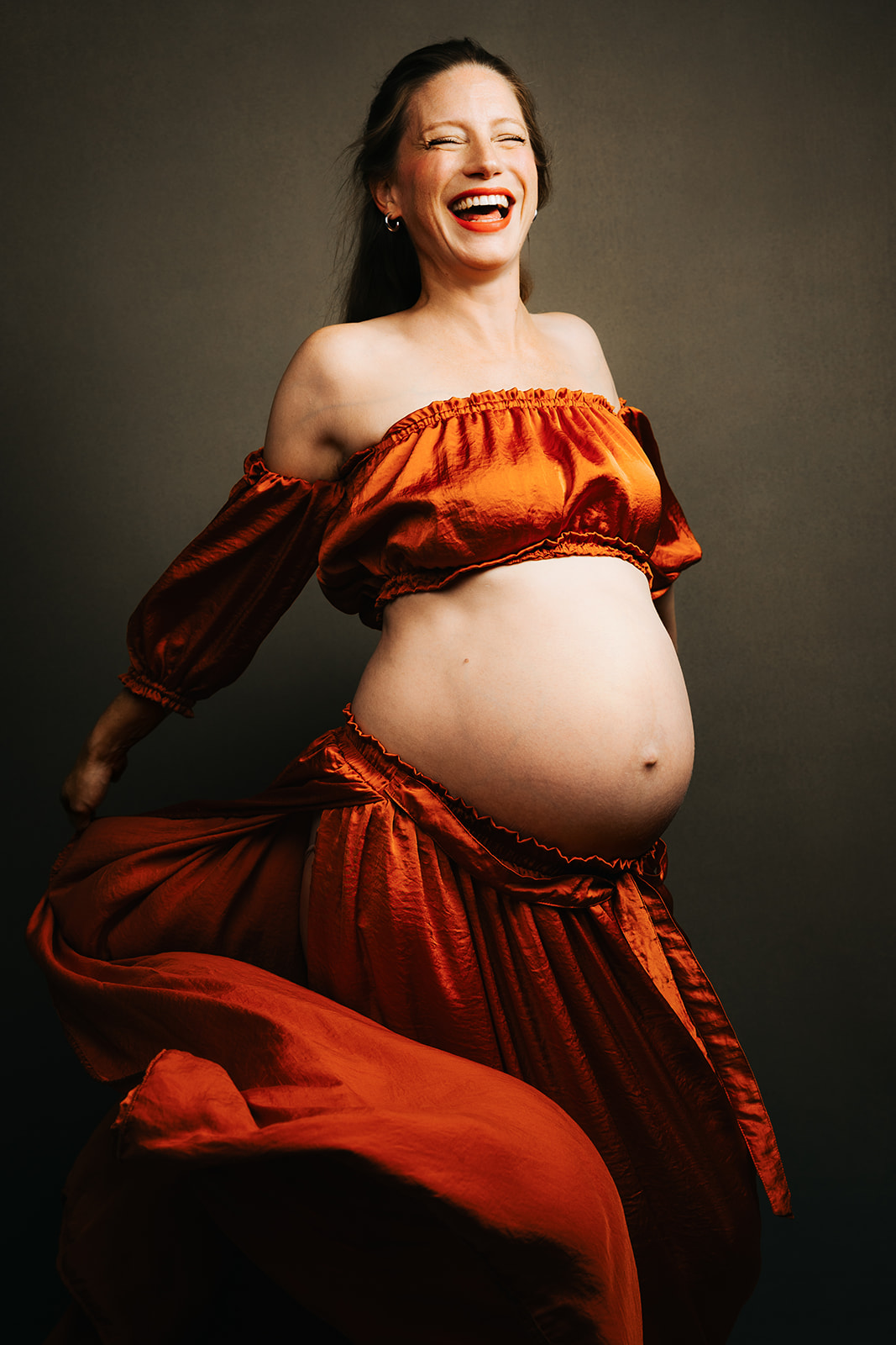 A soon to be mom laughs and smiles while playing with her skirt in a studio after a session of pelvic floor therapy in cambridge, MA.