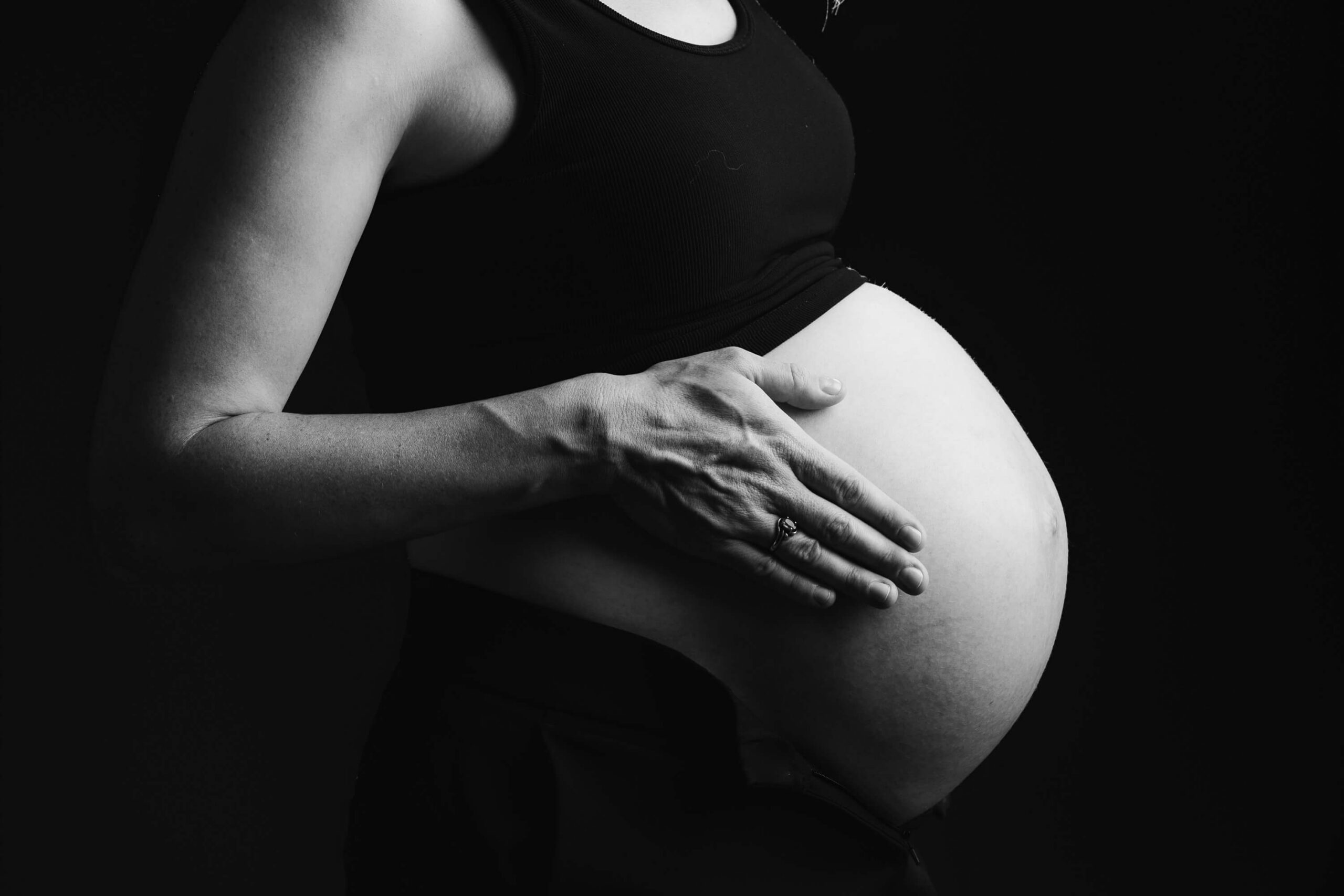 Black and white image of a soon to be mom resting her hand on her bare stomach in a studio after a session of pelvic floor therapy in cambridge, MA.