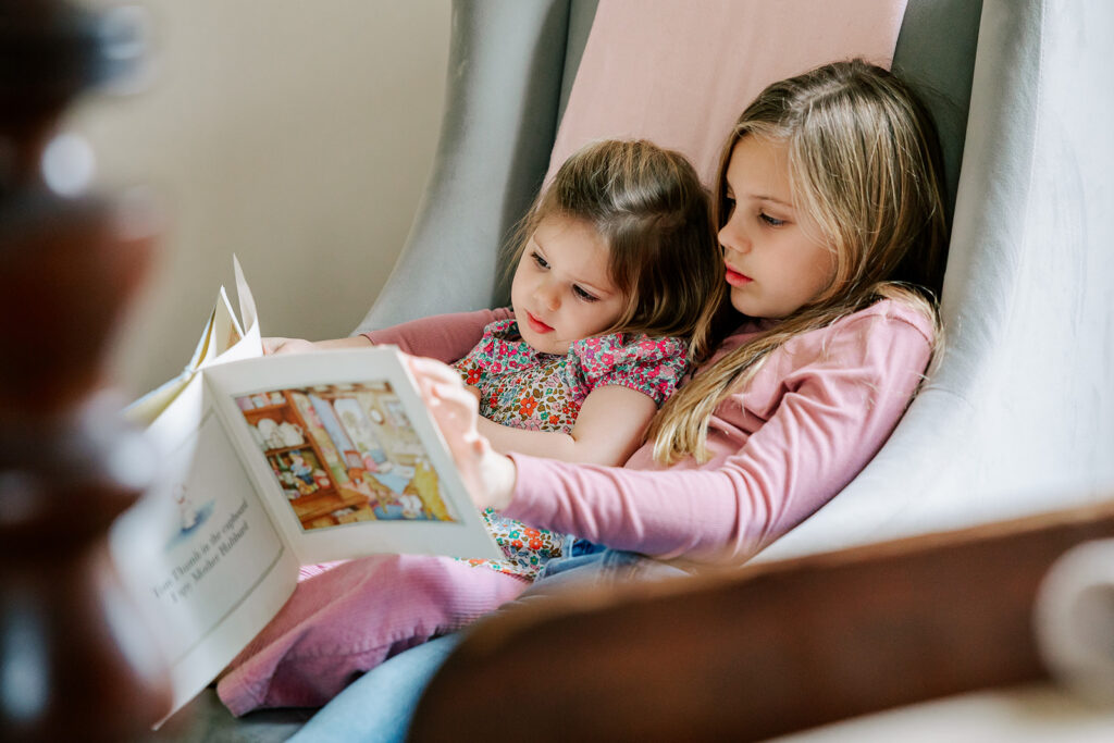 Two girls wearing pink shirts are reading a picture book in a chair after participating in toddler yoga in Boston.