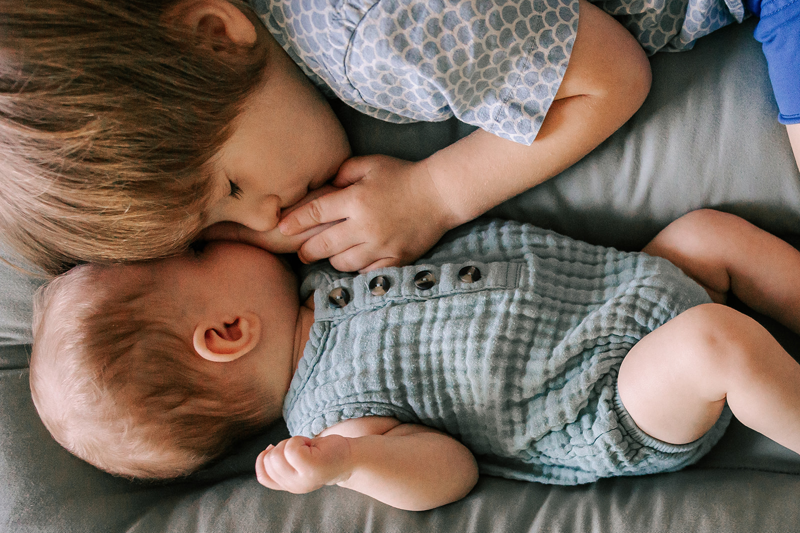 A young boy snuggles with his sleeping baby brother on a bed