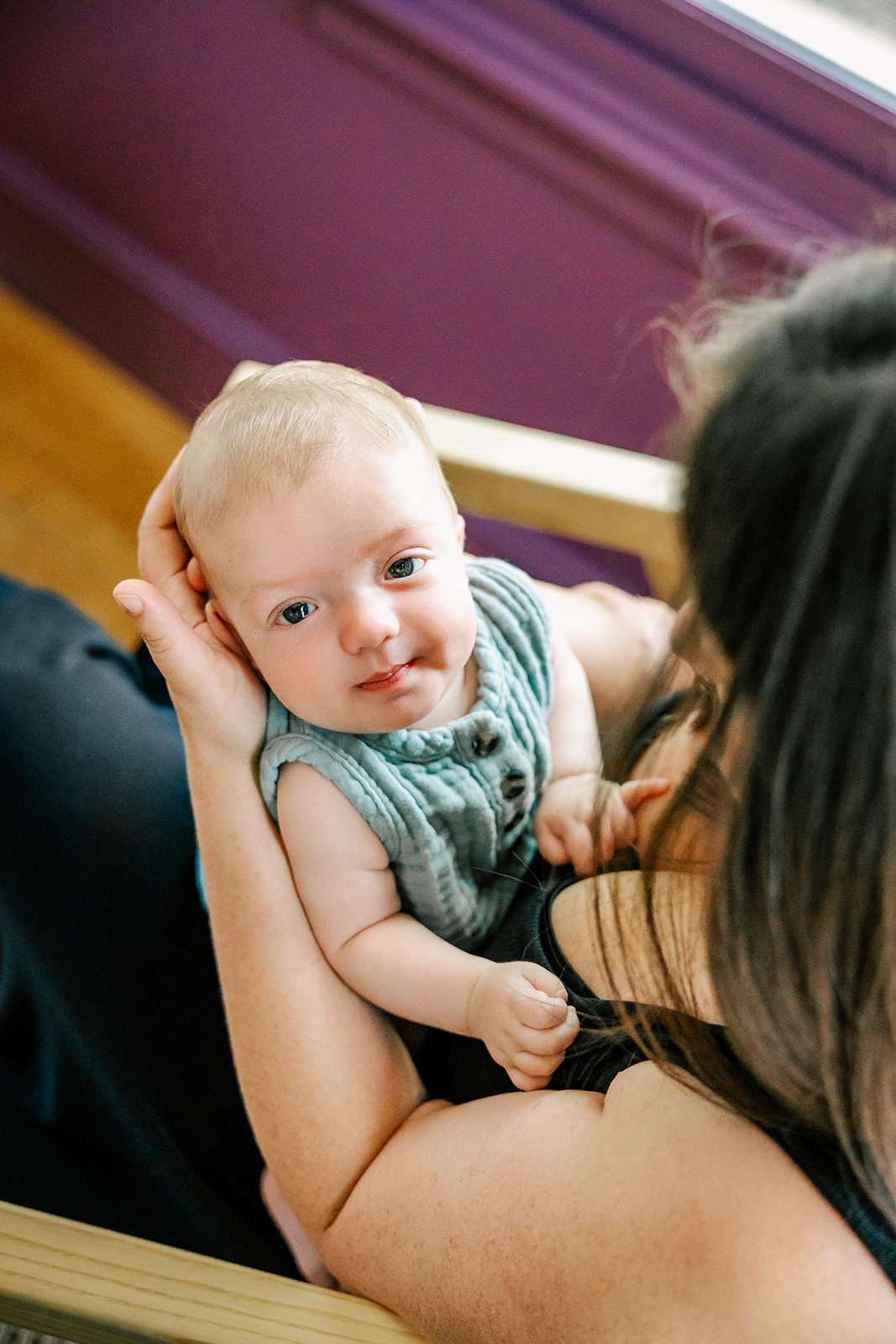 A happy baby sitting in mom's arms and lap looks up in a green onesie after visiting Joy Street Boston