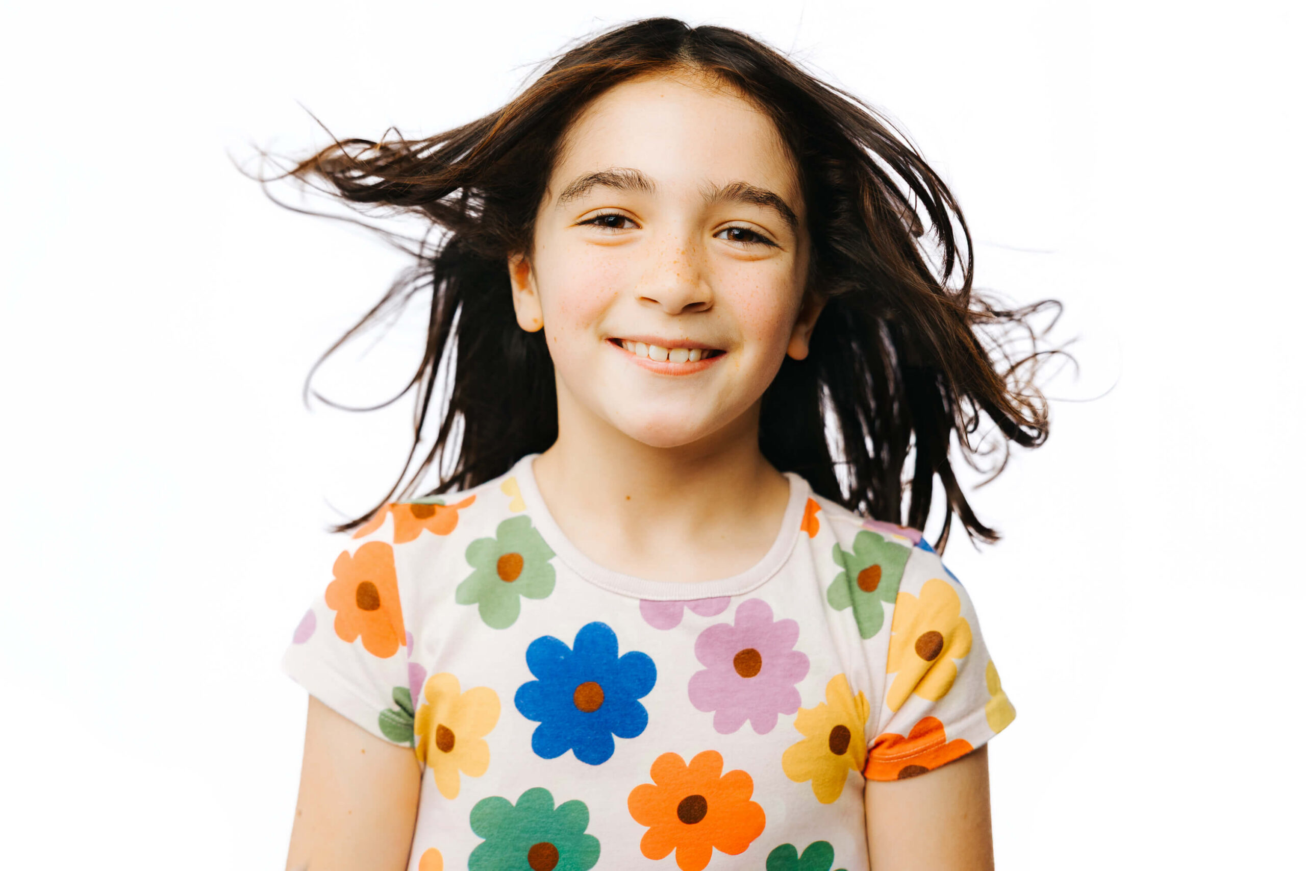 Smiling 7 year old girl with a simple white backdrop; wind blowing back her hair